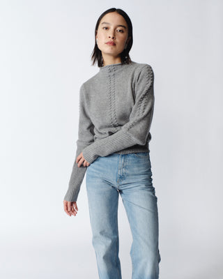Person wearing a gray knitted sweater and blue jeans against a light background.