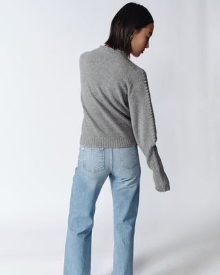 A woman with short hair wearing a gray sweater and blue jeans, facing away from the camera.