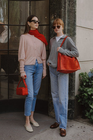 Two women standing outdoors, one with a Garin silk / cashmere cardigan and a red scarf, against a building background.