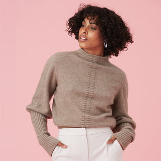 Model wearing a stylish beige sweater against a pink background.