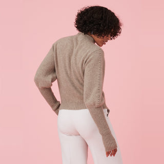 Person wearing a cozy beige sweater with a high collar, facing away against a pink background.