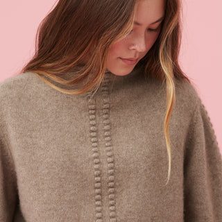 Close-up of a person wearing a cozy brown sweater against a pink background.