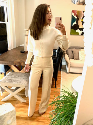 A woman in a stylish white outfit stands in a well-decorated living space.